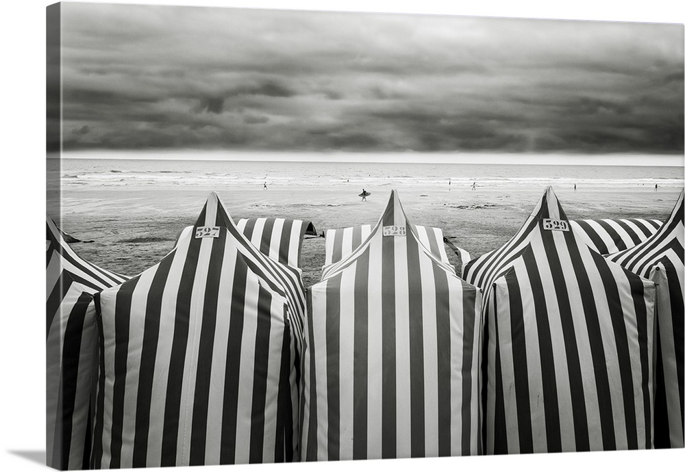 Black and white photograph of  striped beach tents and the ocean in the background at a beach in Spain.