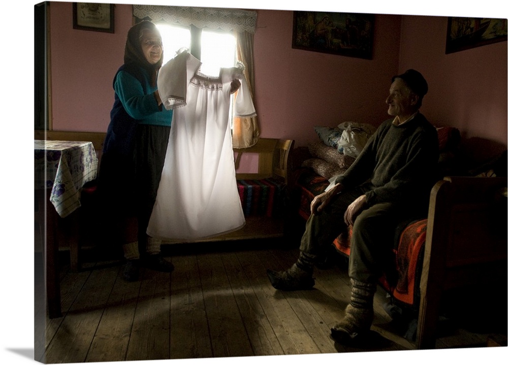 A woman holds up a white dress to show her husband.