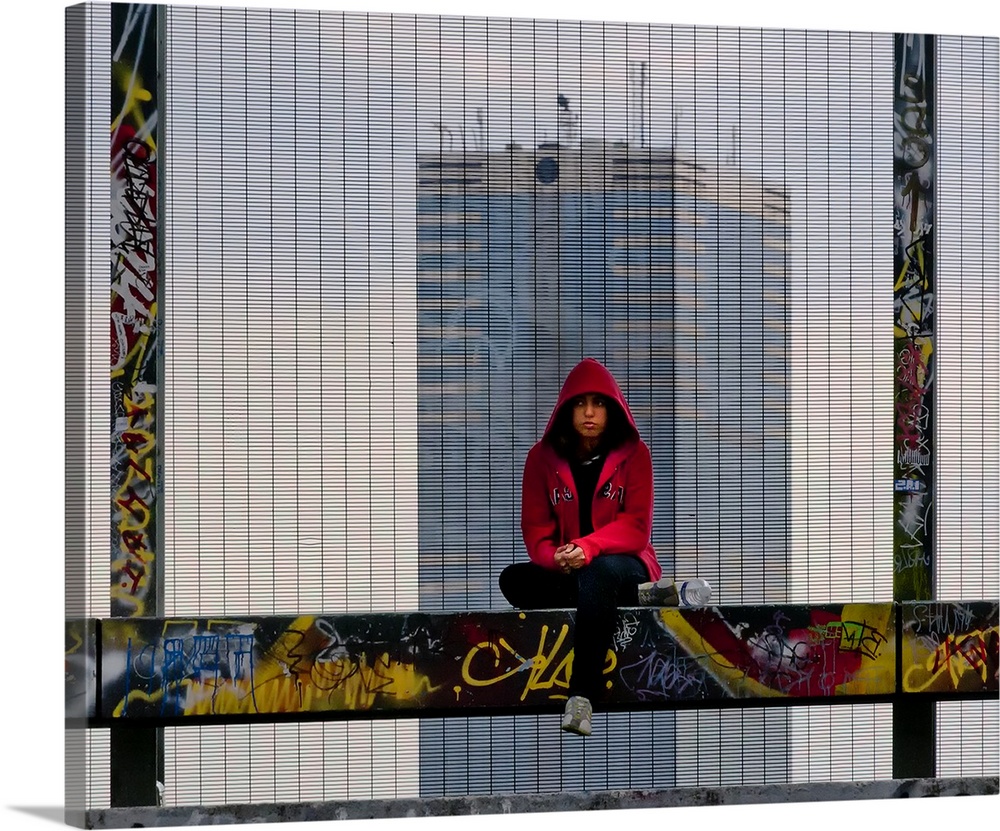 Person sitting on a graffiti-covered railing with a skyscraper directly behind them.