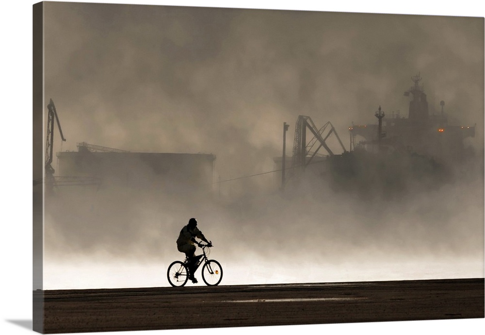 Silhouette of a cyclist in front of smoke coming from the harbor.