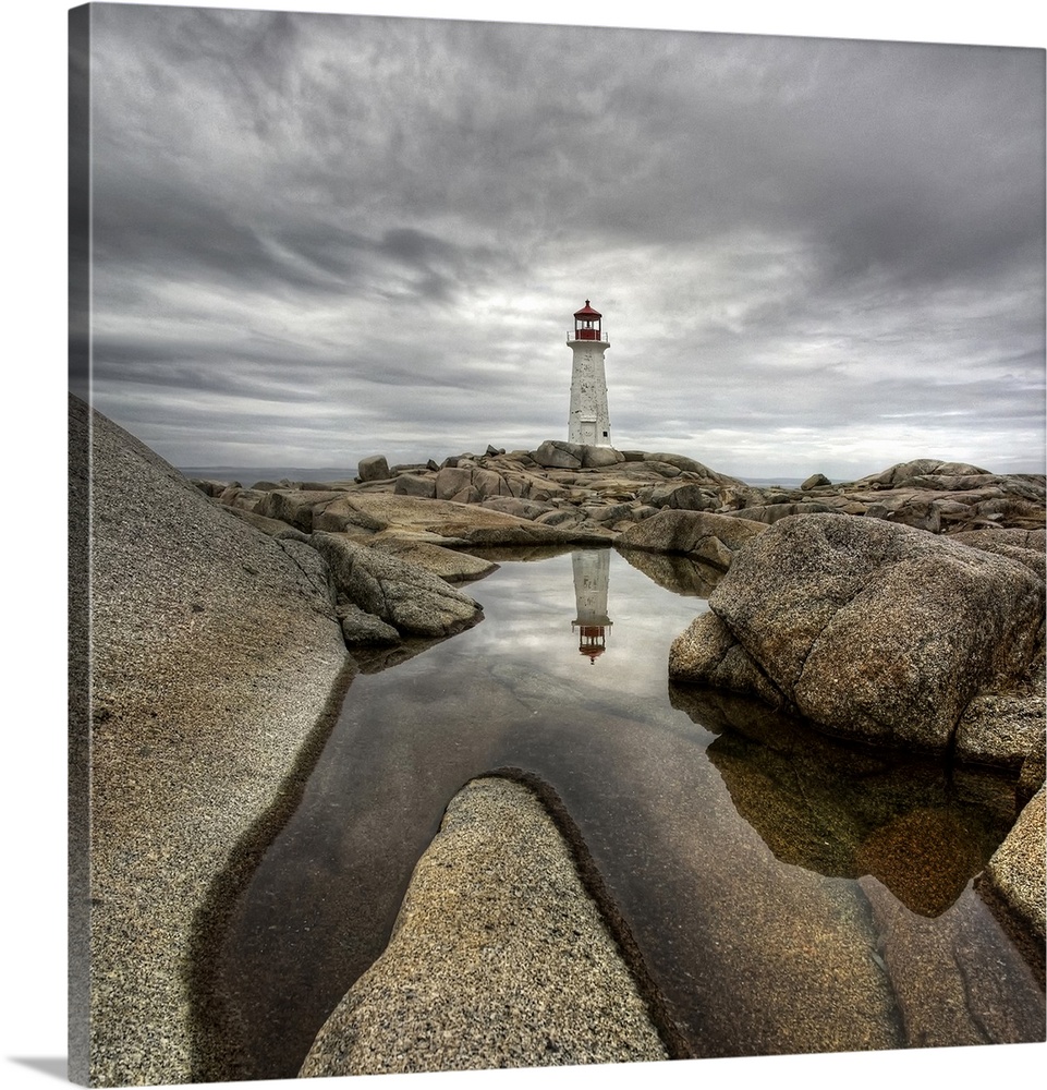 A distant Canadian lighthouse casting its reflection in a rocky tidal pool in the foreground.
