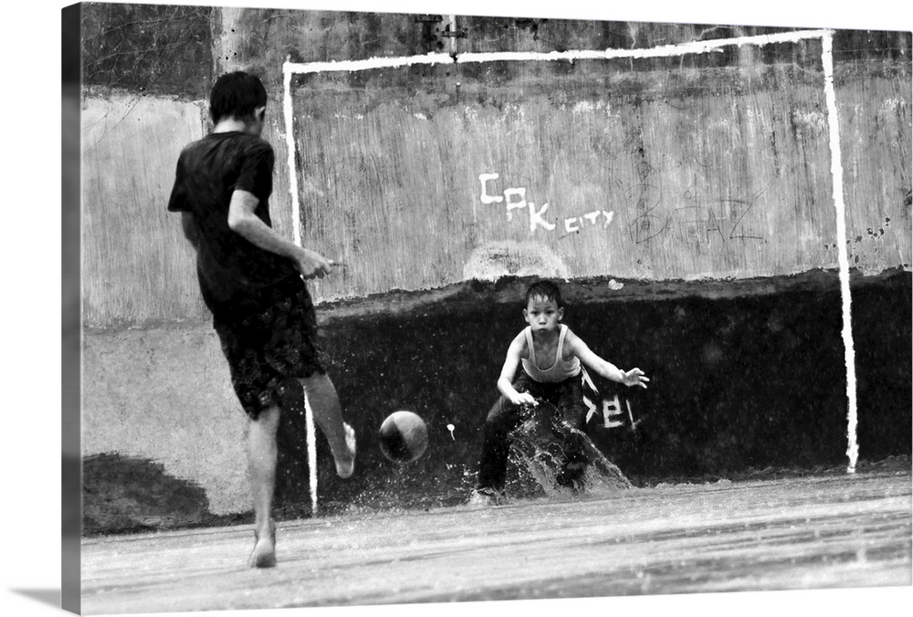 Two boys kick a soccer ball near a makeshift goal.