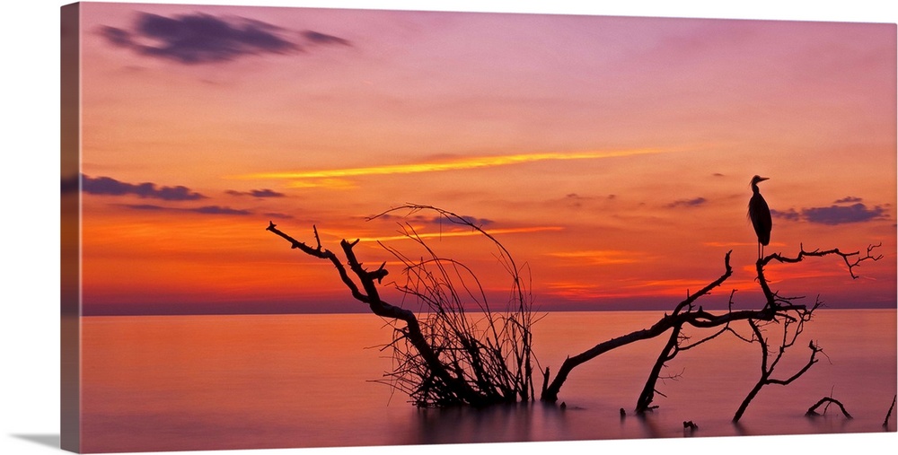Landscape photograph of a beautiful orange, red, yellow, purple and pink sunset over calm water.