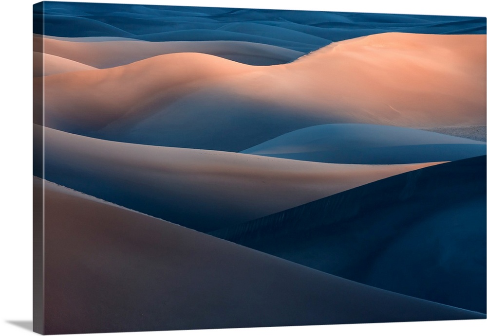 A desert landscape with tall blue and orange sand dunes in the evening.