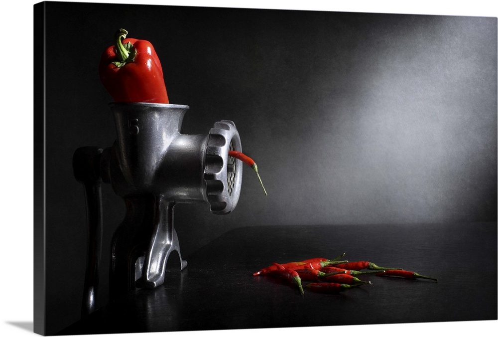 A red bell pepper in a meat grinder with small red chili peppers coming out.