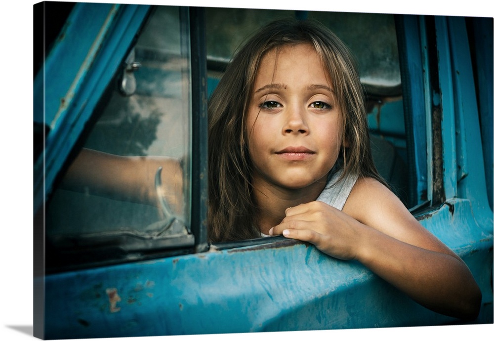 Portrait of a young girl leaning out the window of a blue car.