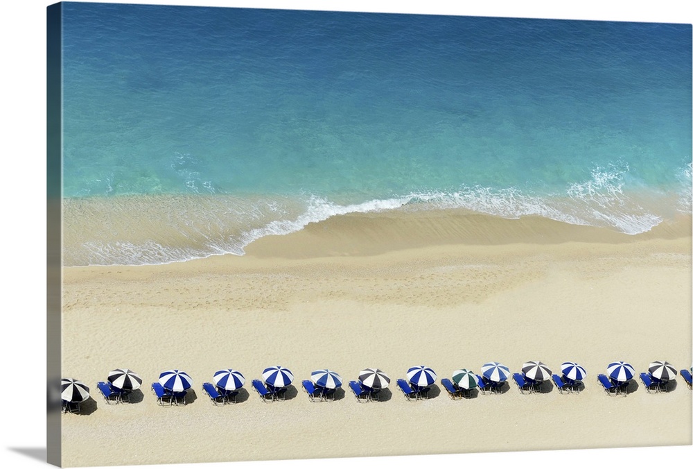 Aerial view of umbrellas lined up close to the water on a beach.