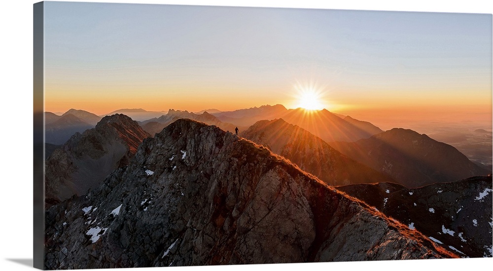 A man running on the ridge of a mountain as the sun rises over the peaks, Stol, Slovenia.