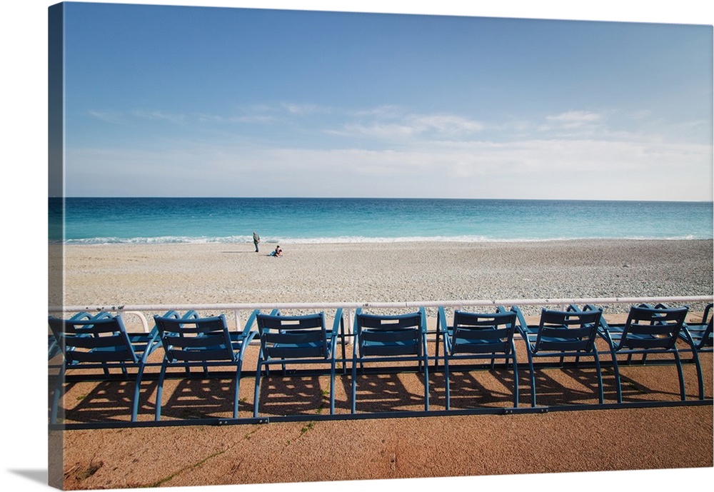 Landscape photograph of the ocean shore with a row of blue beach chairs.