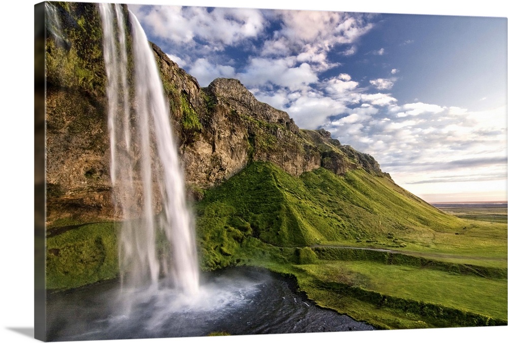 Waterfall on the side of a cliff in a lush valley in Iceland.