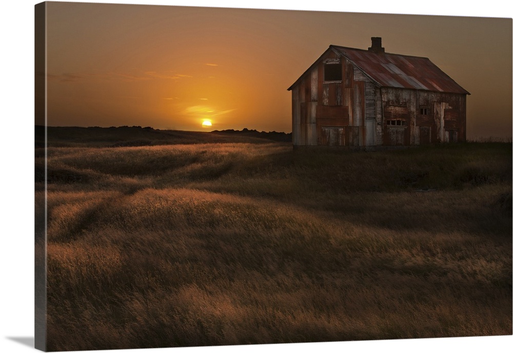A rusted abandoned house in a grassy landscape at sunset, Iceland.