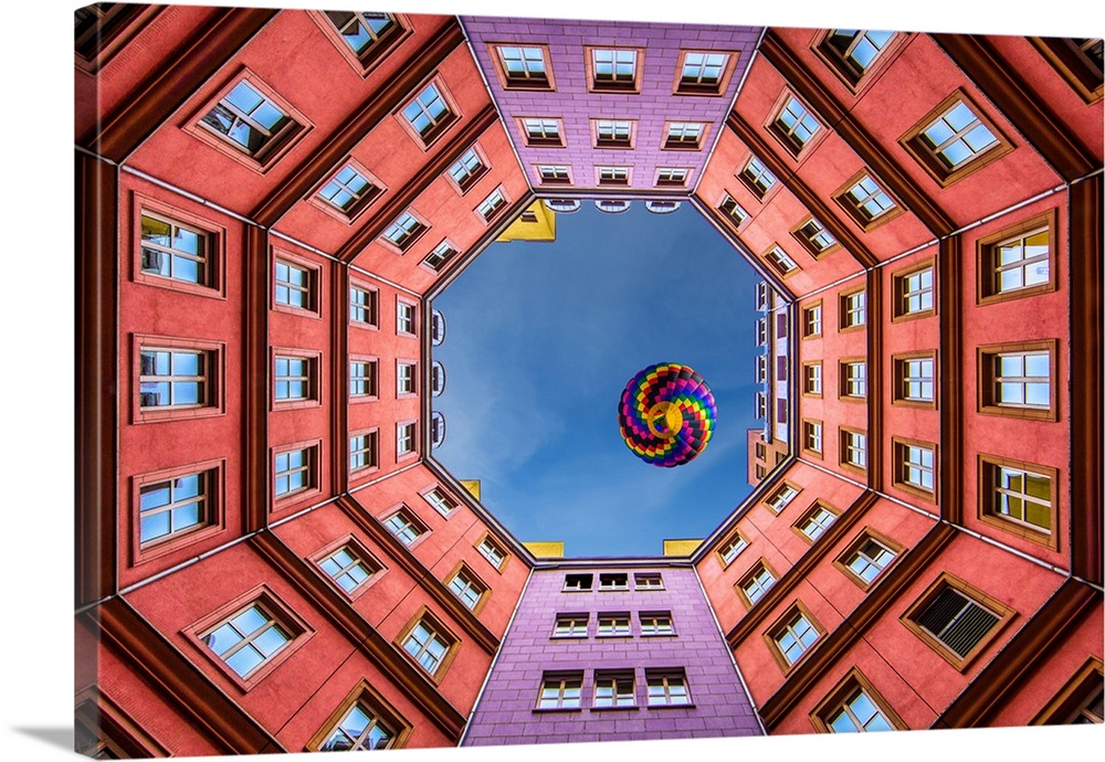 Photograph looking up from the middle of a courtyard at a colorful hot air balloon.