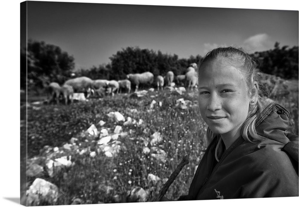 A young girl in Turkey smiles with her flock of sheep behind her.