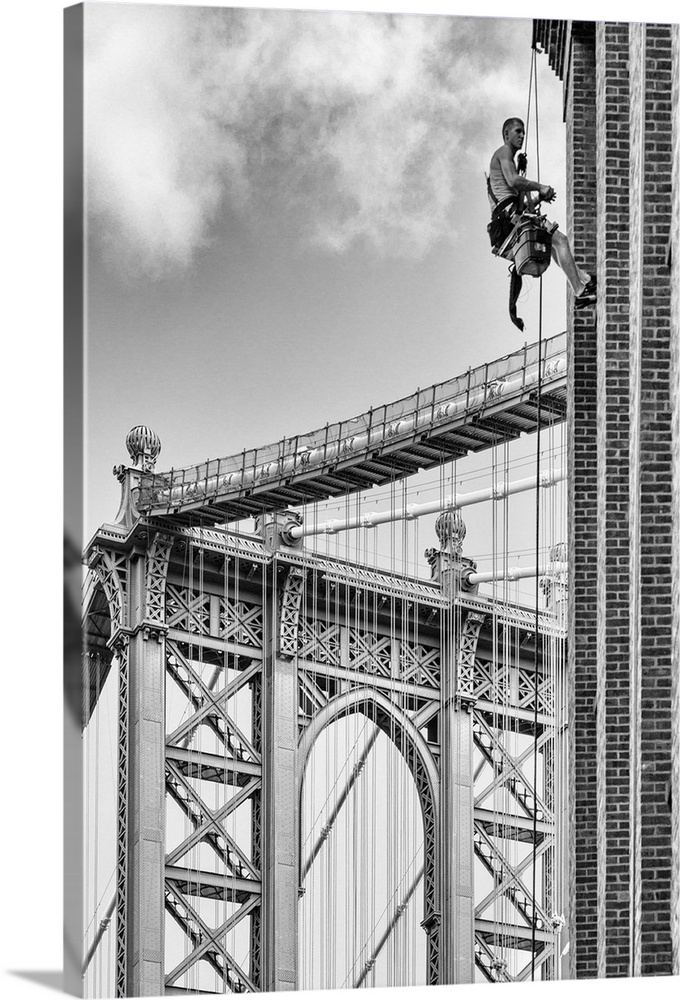 A black and white photograph of a man in harness hanging from a building with the Manhattan bridge in the background.