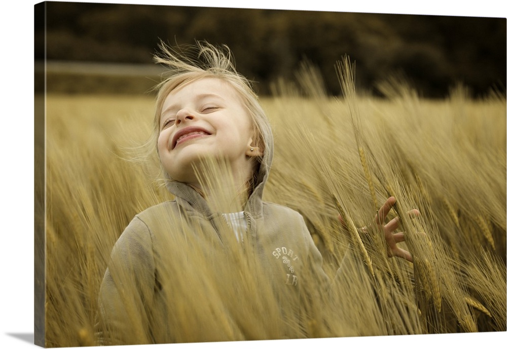 A young girl happily smiles as a breeze blows stalks of wheat around her.