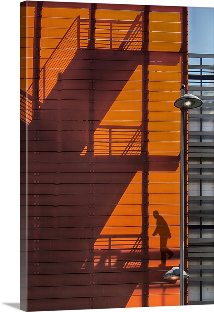 Shadow of a fire escape staircase and a person walking down cast onto the side of an orange building.