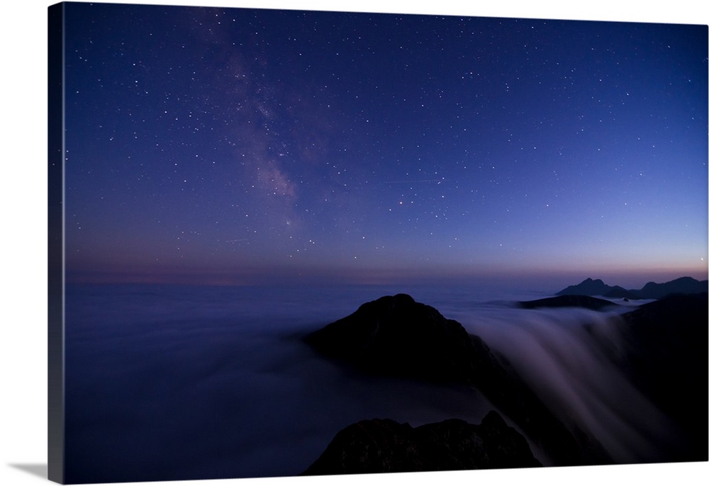 Skyscape in the evening with stars, above a misty mountain range.
