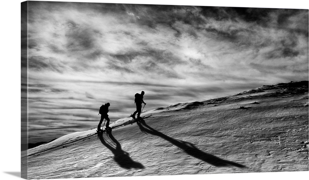 Silhouettes of two people trekking up a mountain.