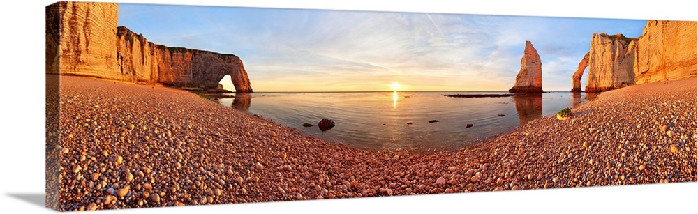 Panoramic view of the sun setting on the horizon from the rocky beach of Etretat, France.