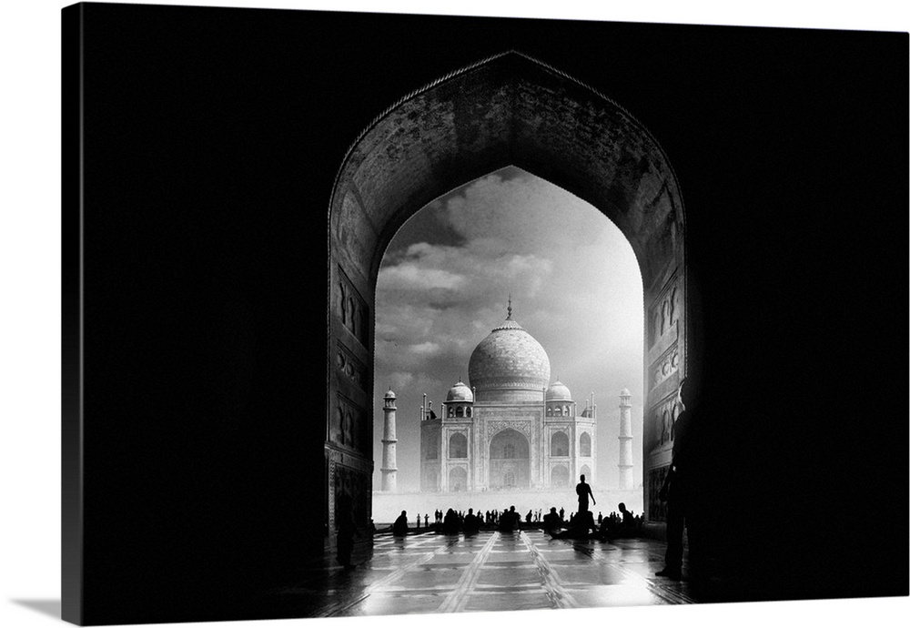 The Taj Mahal with low lying fog seen through an arch shrouded in darkness.