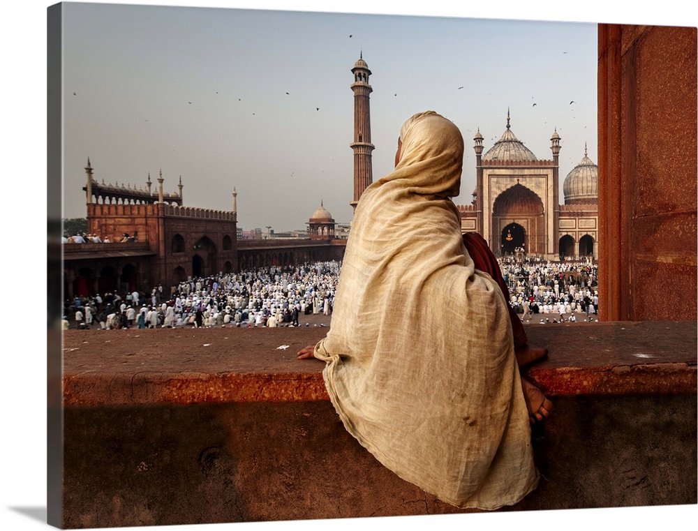 A person wearing a robe, sitting on a ledge, overlooking a crowd, India.