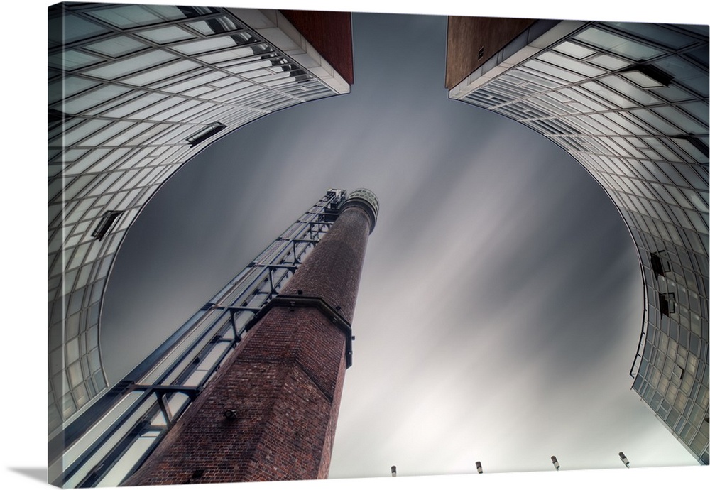 Abstract view of a chimney in a factory framed by curved buildings.