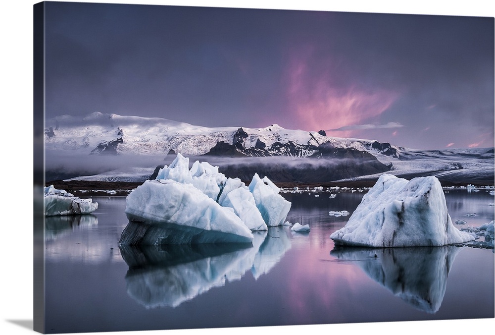 Large glaciers in the water with snowy mountains in the distance under a pastel-colored sky, Jokulsarlon, Iceland.