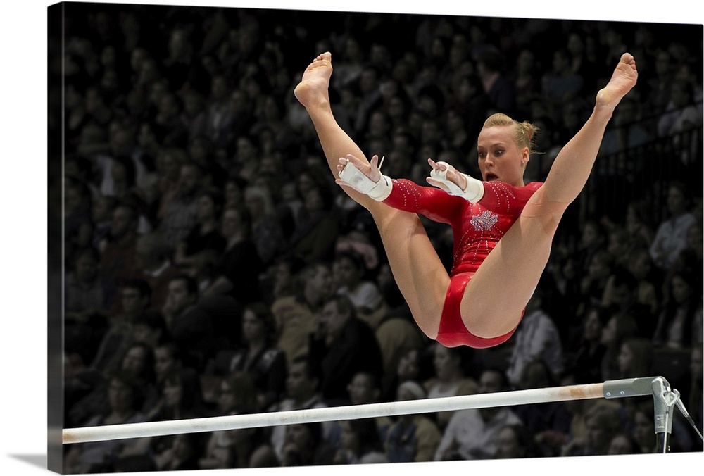 A female gymnast flies over the high bar with her legs raised up, arms outstretched ready to grab the bar.