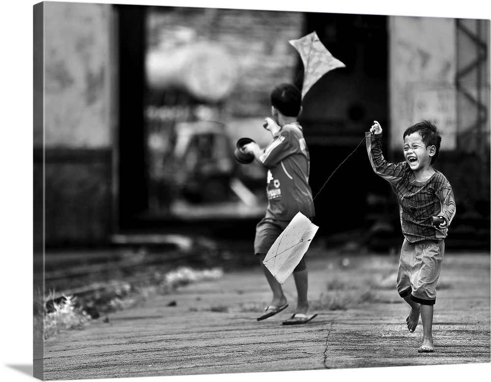 Two young boys pull kites behind them as the run down a street.