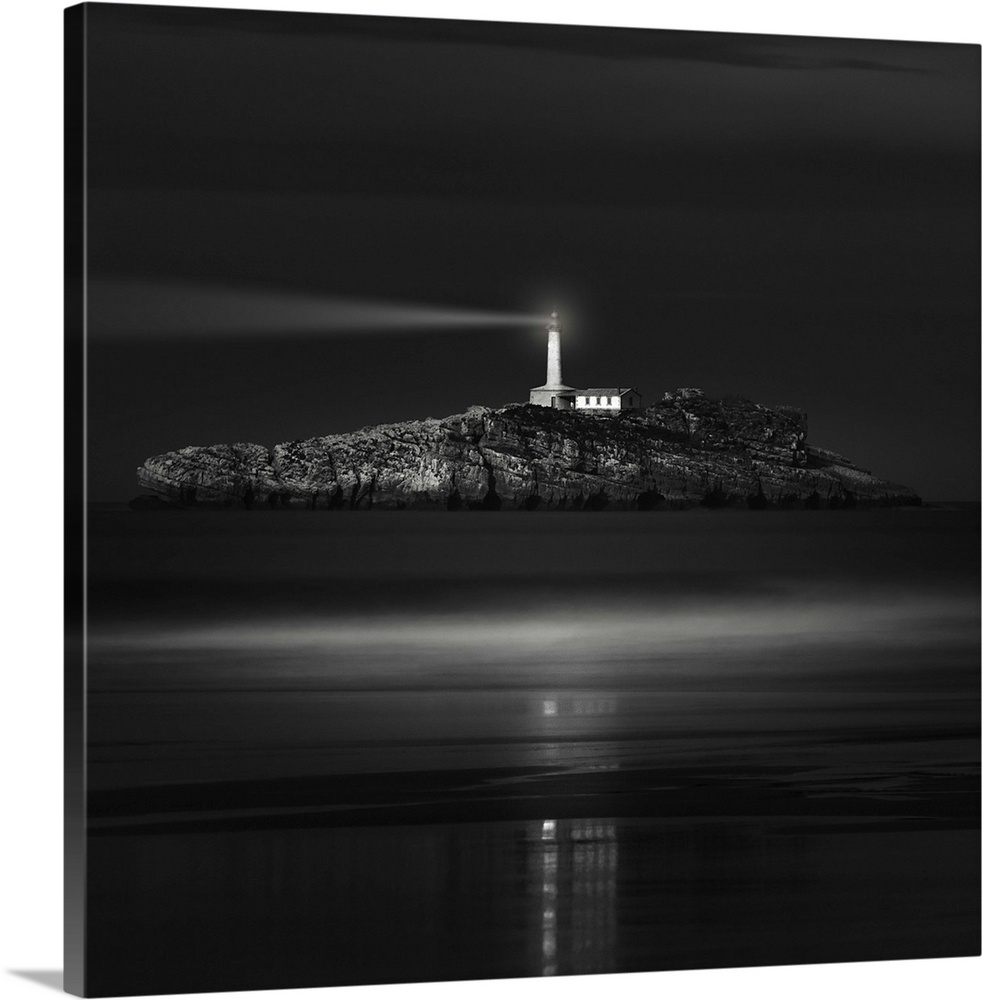 A lighthouse on a rocky island in the ocean shines a bright light into the night.