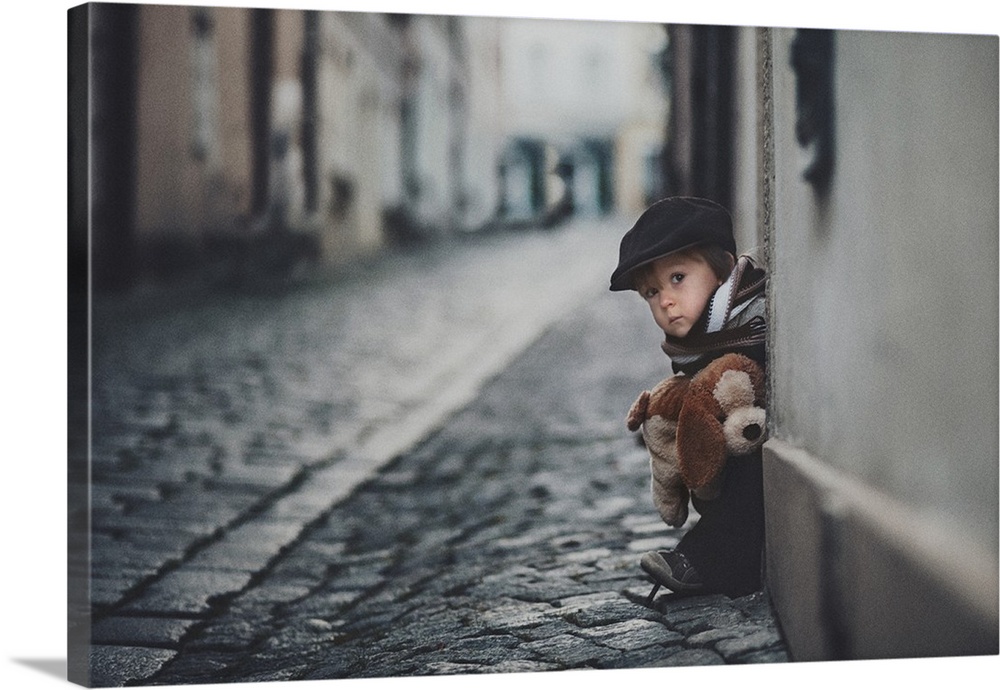 A portrait of a little boy sitting on a doorstep on a cobblestone road.