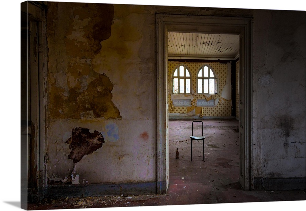 Interior photograph of an abandoned room with paint peeling from the walls, dirt on the floor, and a lone chair with a bot...