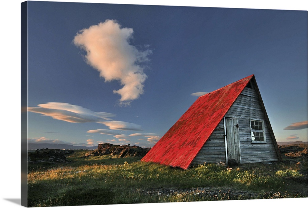 a wooden hut in Iceland with a bright red roof, seen at sunset.