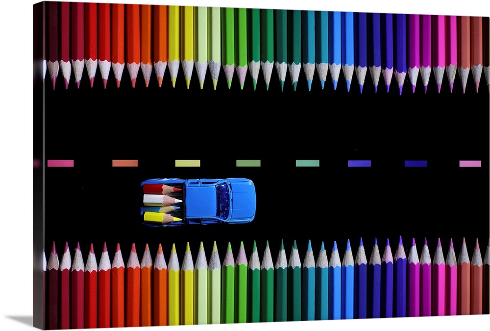 Conceptual photograph of a two truck hauling tiny colored pencils like lumber along a colored pencil lined road.