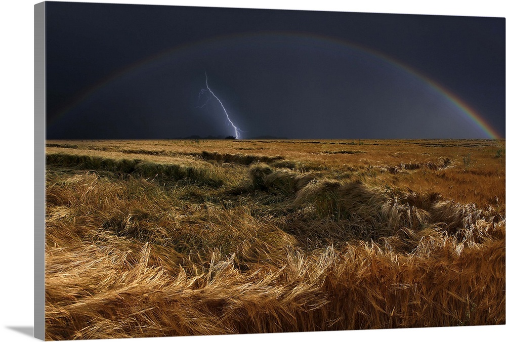 Field after storm with a rainbow in the dark sky and one final bolt of lightning.