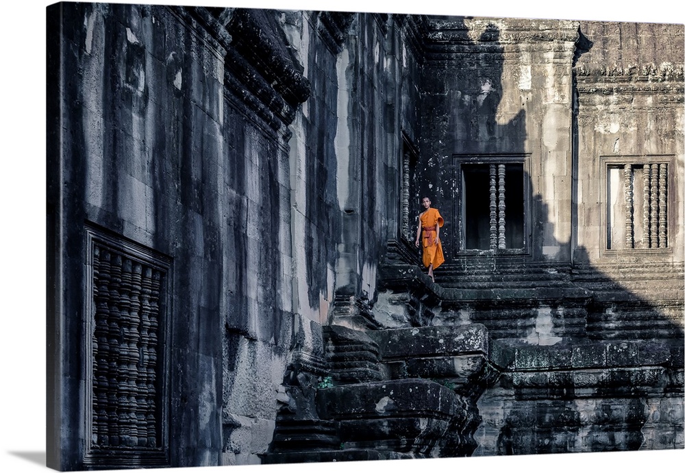 A monk's orange robes make him stand out against the shadows at Angkor Wat.