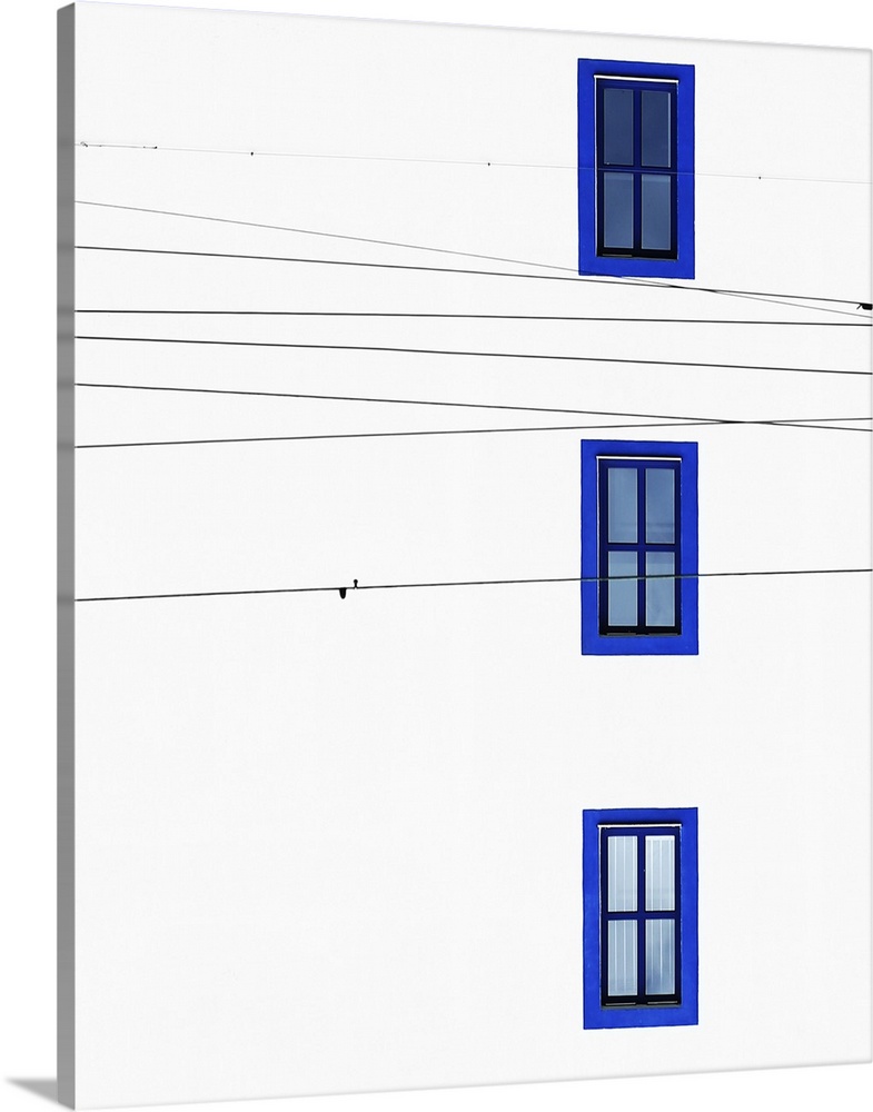 The wall of a building with three windows with blue frames and intersecting power lines.