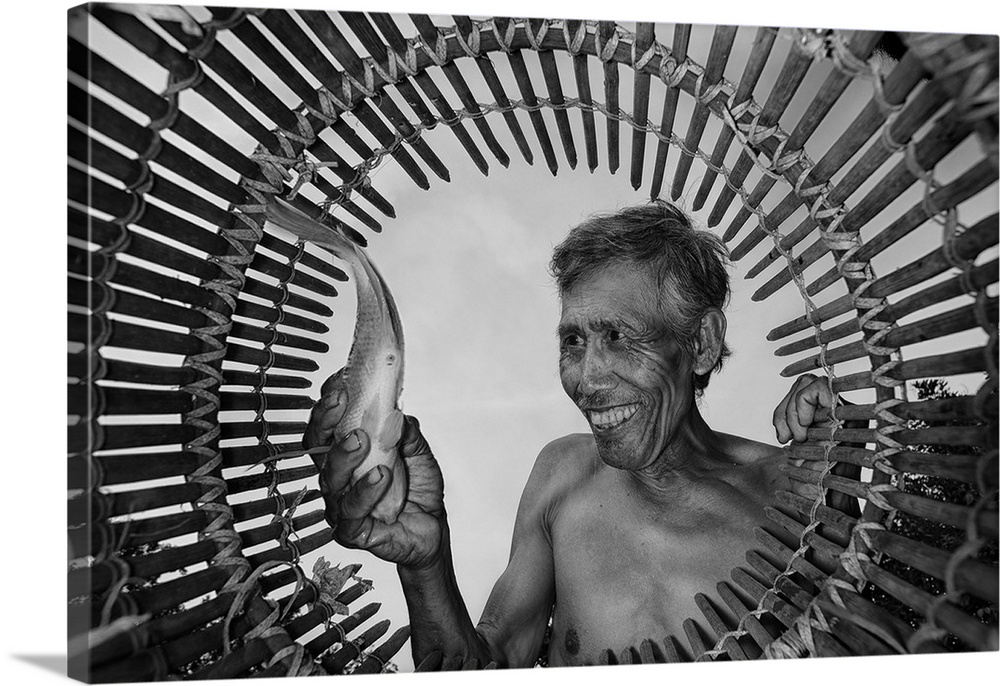 A fisherman happily pulls a fish out of a bamboo basket.