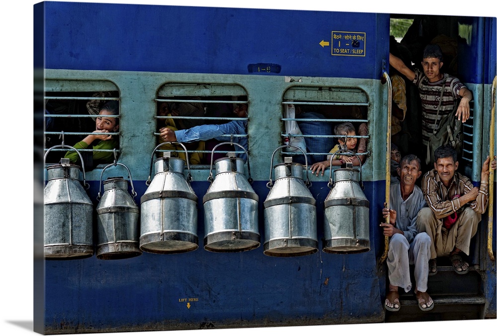 Passengers in the door and windows of a train in India, with milk cans hanging on the sides.