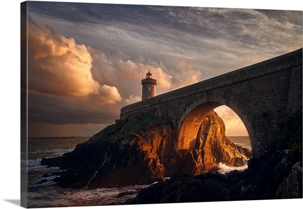 Warm photograph of a rocky bridge over the ocean with an orange sunlit tunnel and a lighthouse on the end at sunrise.