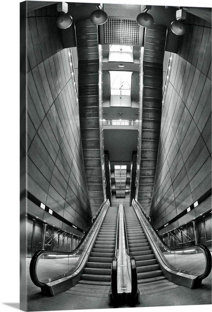 Black and white image of escalators in a station, with a view of the skylights in the ceiling.