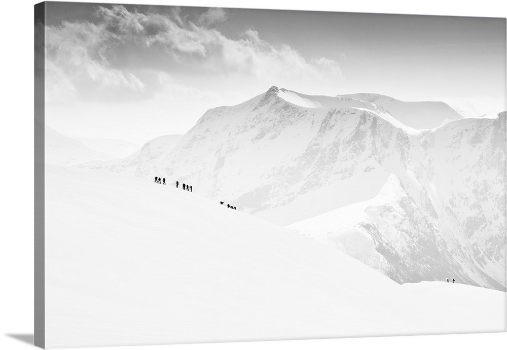 Small figures walking up a completely snow-covered mountain with snowy peaks in the distance, Veirhaldet, Norway.