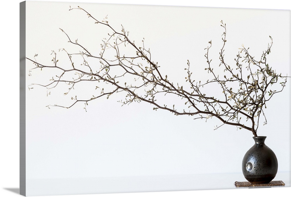 Still life photography of a branch with several small flowers in a round vase.