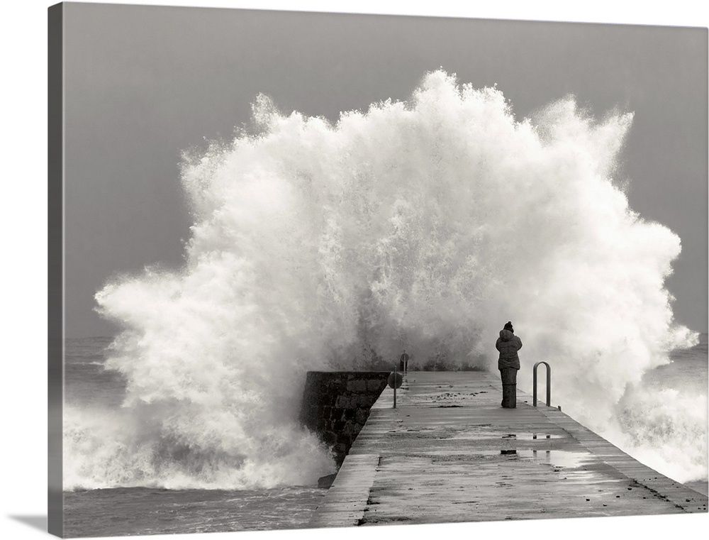 A photographer standing on a pier with waves crashing.