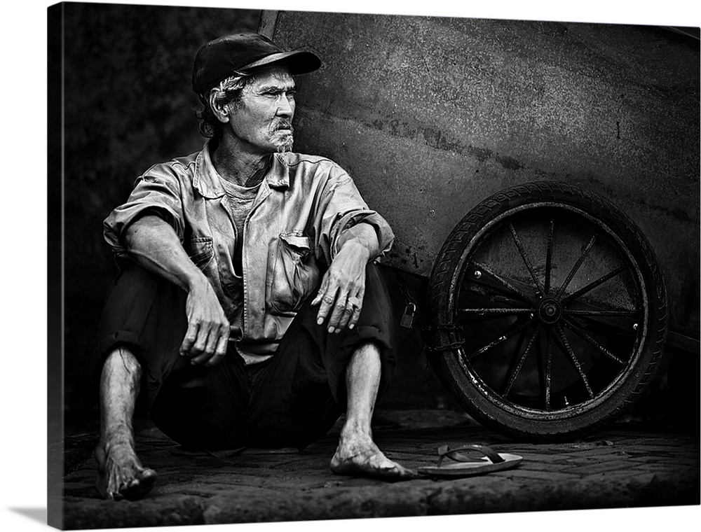 A barefoot man sitting in the street next to the wheel of his wagon in Jakarta, Indonesia.
