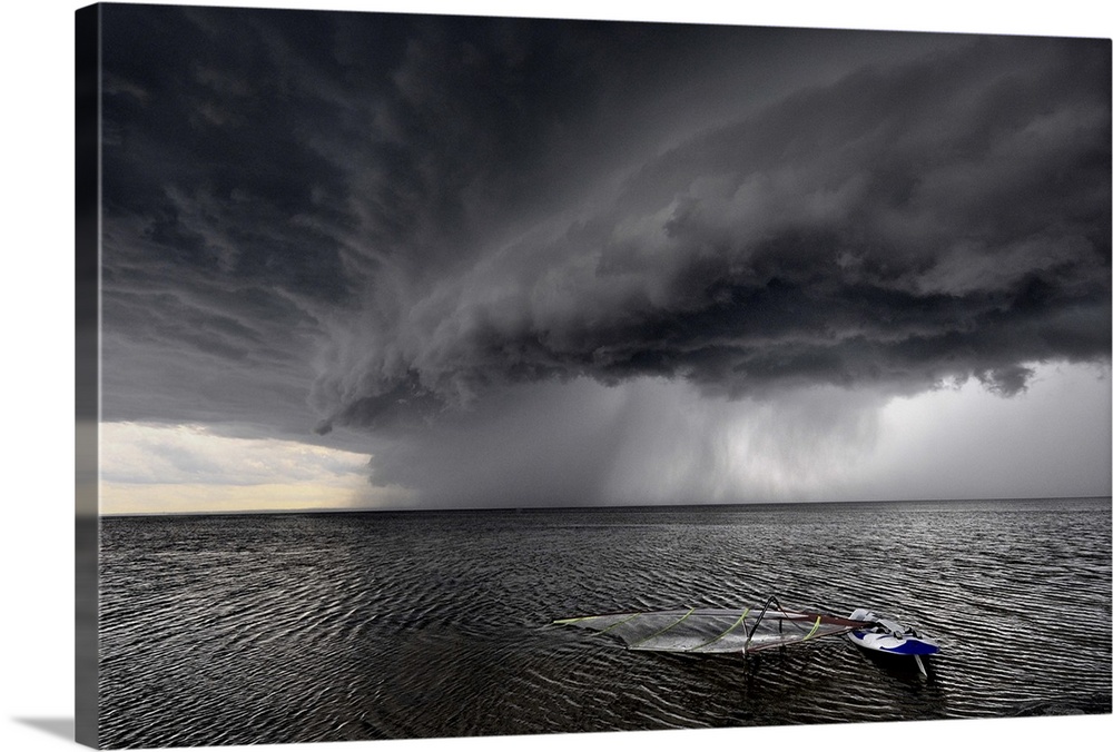 A windsurfing board lays flat in the water as stormclouds with heavy rain approach.