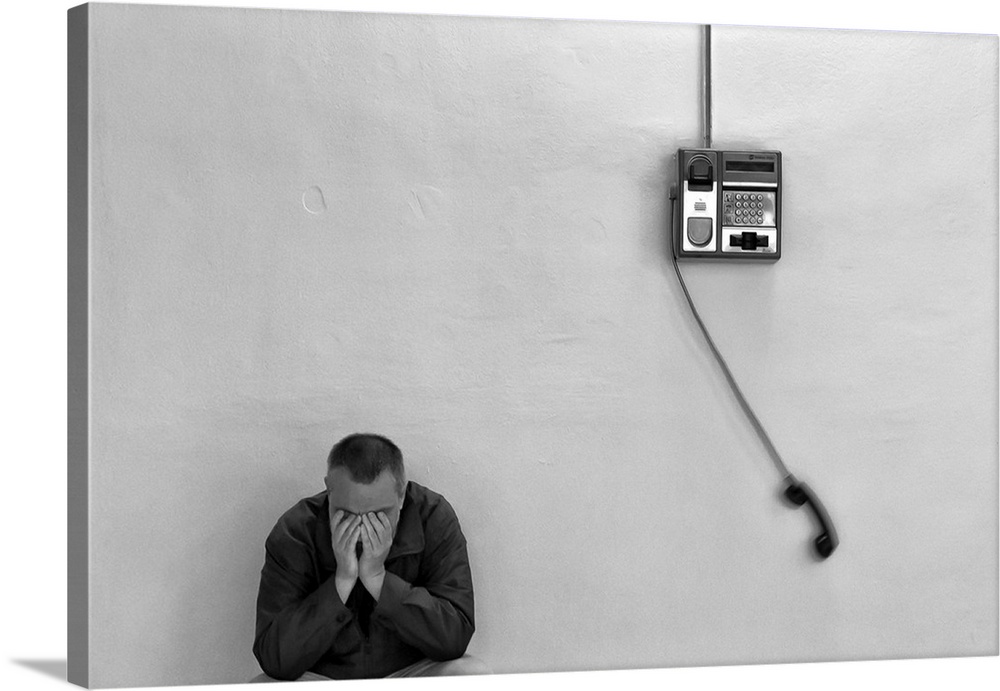 A man with his head in his hands leaning against a wall with a payphone swinging from the receiver.