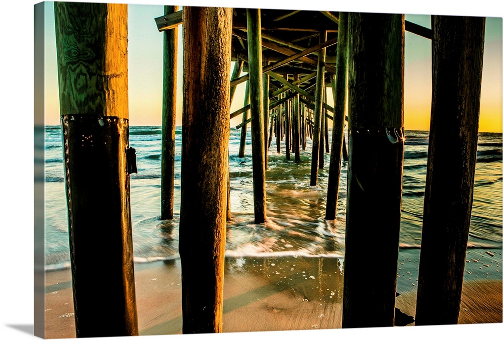 A photograph looking through the underside of a long pier out over the ocean. The sky glowing with morning sunlight.