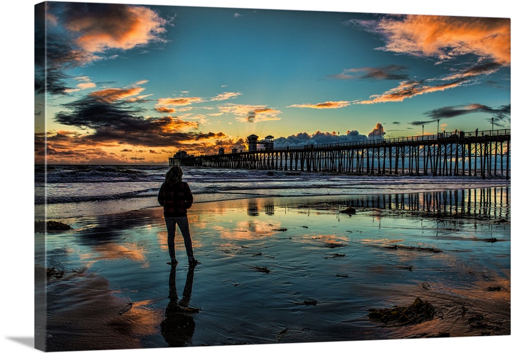 A woman stands in reflective sands near the Oceanside Pier, Oceanside, California, USA.