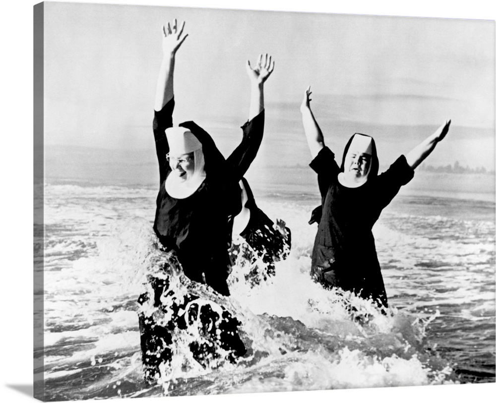 1950s Three nuns wearing habits laughing jumping in ocean surf.